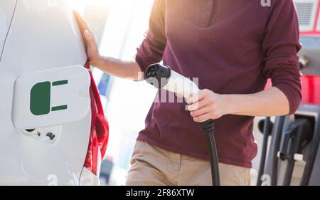 Un homme se tient près d'une voiture électrique et tient un fiche de charge Banque D'Images