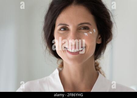 Photo de tête portrait femme souriante avec lotion hydratante sur joue Banque D'Images