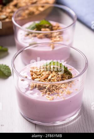 Gros plan de deux verres de yaourt aux baies avec céréales sur une table blanche rustique. Banque D'Images