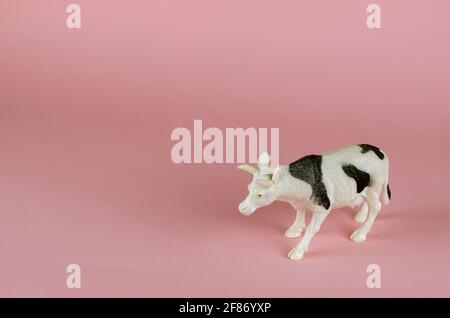 Figurine d'une vache sur fond rose. Animal blanc avec taches noires. Élevage de bétail, concept d'agriculture. Copier l'espace. Vue latérale inclinée. Banque D'Images