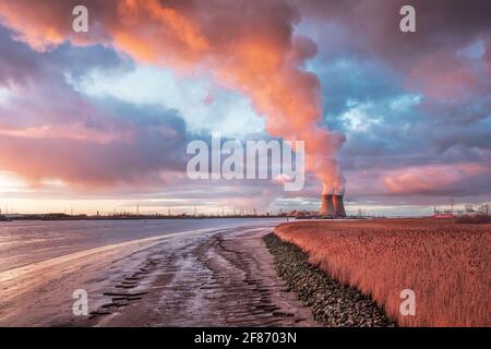 Paysage industriel avec des nuages spectaculaires vus du quai de la rivière Escaut avec centrale nucléaire Doel sur le fond et de grands panaches de vapeur. Banque D'Images