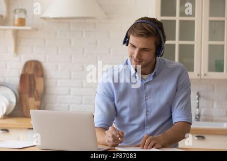 Homme motivé dans le casque, regardant un webinaire, prenant des notes, utilisant un ordinateur portable Banque D'Images