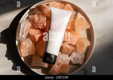 Tube sans marque avec cosmétiques de soins du corps se trouve sur des cristaux de sel himalayan rose. Concept spa et puits de puits. Banque D'Images