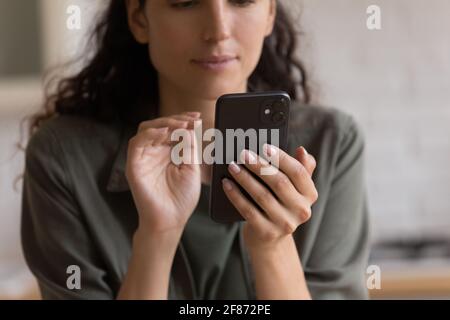 Une femme en gros plan regarde l'écran d'un ordinateur portable, tenant son smartphone Banque D'Images