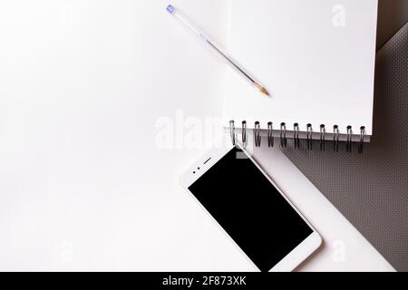 Arrière-plan blanc avec un smartphone, un ordinateur compact, une note et un stylet sur le bureau insolé. Banque D'Images