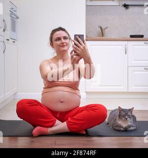 Des cours de fitness pendant la grossesse et des vidéos d'exercice de tir pour un blog en ligne. Une femme enceinte à une séance d'entraînement sportif dans la cuisine prend un Banque D'Images