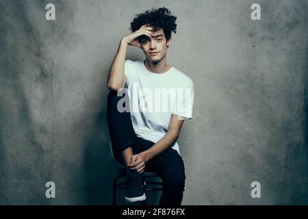 homme en t-shirt blanc est assis sur les chaises mode cheveux bouclés style de vie Banque D'Images