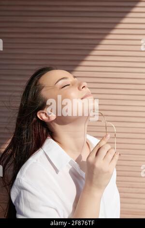 Belle jeune femme souriante avec une peau parfaitement lisse qui s'envole lunettes de soleil et profiter de la lumière du soleil Banque D'Images