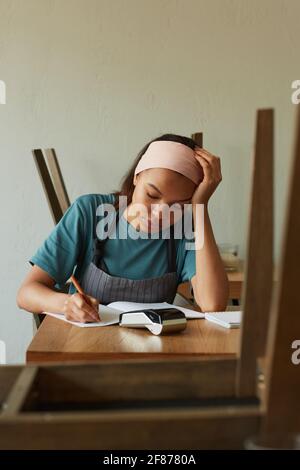 Portrait vertical de la jeune femme afro-américaine calculant les finances et faire l'inventaire dans la petite boutique d'entreprise Banque D'Images