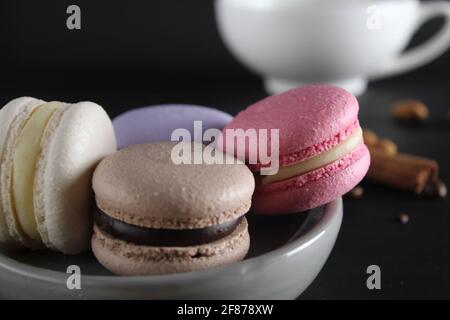 Macarons sur l'assiette à l'arrière tient une tasse de café ou de thé grains de café et cannelle sur fond noir avec un lieu pour le texte . Banque D'Images