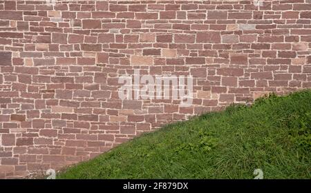 Vieux mur en grès rouge derrière une colline d'herbe Banque D'Images