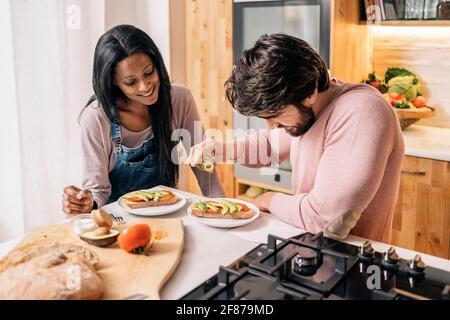 Gaie femme noire et son petit-ami ayant délicieux petit-déjeuner méditerranéen dans la cuisine à la maison. Banque D'Images