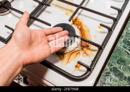 La main de Guy pointe à un brûleur de cuisinière à gaz sale après la cuisine à la maison dans la cuisine. Banque D'Images