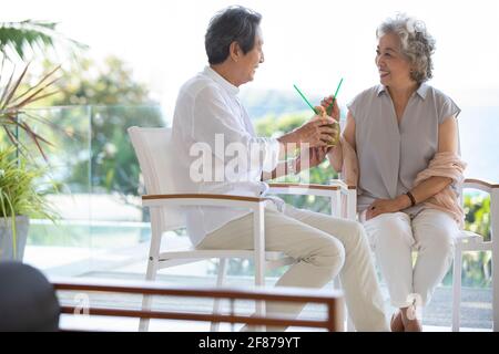 Bon couple senior qui boit du lait de coco sur le balcon Banque D'Images