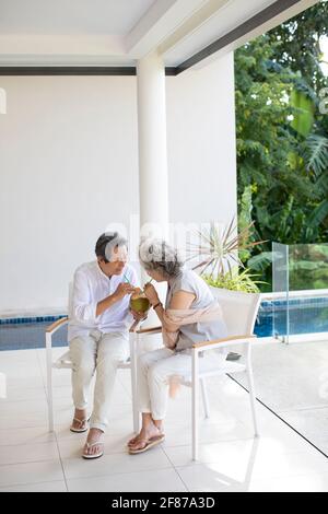 Bon couple senior qui boit du lait de coco sur le balcon Banque D'Images