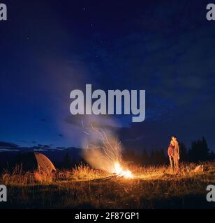 Ciel étoilé de nuit sur une colline herbeuse avec tentes de camp, feu de camp et randonneurs. Les jeunes voyageurs, hommes et femmes, profitent de la vue sur le ciel bleu nocturne. Concept de relation, de camping de nuit et de voyage. Banque D'Images