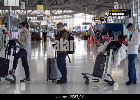 Bangkok, Thaïlande - 11 avril 2021 : passagers asiatiques utilisant un smartphone pour vérifier les nouvelles et attendant de suite pour s'enregistrer pour des vols d'avion en Covid- Banque D'Images