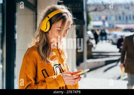 Portrait en gros plan d'une femme caucasienne souriante défilant sur les réseaux sociaux et écoutant du son avec des écouteurs sans fil. Personnes utilisant un fil moderne Banque D'Images