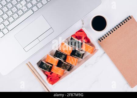 Boîte de livraison blanche avec un ensemble de rouleaux de sushis avec saumon sur fond de table en marbre blanc avec ordinateur portable - futomaki. Uramaki et hosomaki. Cuisine asiatique Banque D'Images