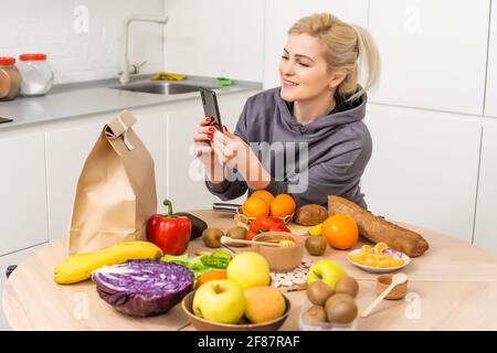 La femme règle les achats dans la cuisine. Livraison de produits d'épicerie dans des sacs en papier. Service d'abonnement de l'épicerie dans des conditions de quarantaine parce que Banque D'Images