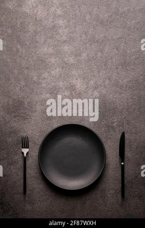 assiette, fourchette et couteau vides noirs sur une table à texture foncée, plat. Un concept pour un restaurant ou un café menu bar Copy espace Banque D'Images