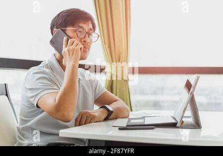 Homme parlant sur un téléphone portable tout en travaillant sur un ordinateur portable. Banque D'Images
