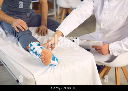 Section médiane de la main du médecin pointant vers le patient blessé cassé jambe en bandage Banque D'Images