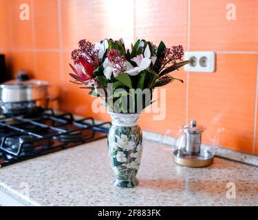 Un bouquet intéressant dans un vase dans la cuisine. Arrière-plan flou, ustensiles de cuisine visibles. Banque D'Images