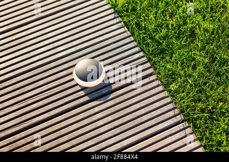 Éclairage extérieur rond noir sur une jetée marron clair avec de l'herbe verte fraîche adjacente. Banque D'Images