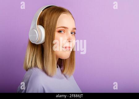 Confiante jeune femme dans le portrait de casque. Belle femme sérieuse avec la coiffure blonde appréciez écouter la musique de chanson dans le casque isolé au-dessus de violet Banque D'Images