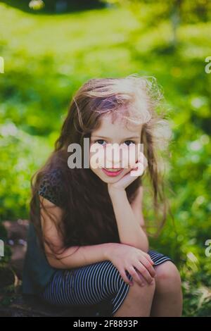 Petite fille en robe sombre avec de longs cheveux assis dans le jardin de printemps Banque D'Images