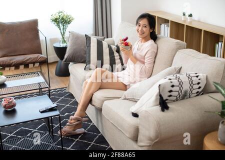 Bonne jeune femme mangeant de la salade de fruits dans le salon Banque D'Images
