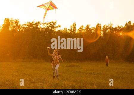 Deux enfants font un cerf-volant au coucher du soleil dans le parc Banque D'Images