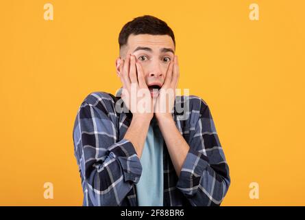 Jeune homme hippster se sentant peur, essayant de cacher son visage sur fond orange studio Banque D'Images