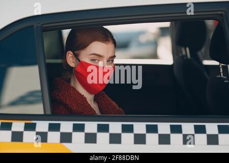 Une jeune femme passager prend un trajet en voiture de taxi pendant la quarantaine pandémique du coronavirus. Femme portant un masque médical stérile. Concept de la distance sociale et de la sécurité sanitaire dans les transports Banque D'Images