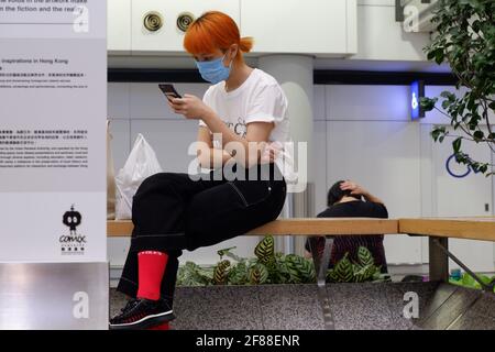 Hong Kong scène à l'intérieur de l'aéroport international HKIA avec une fille en attente sur un banc sur son téléphone Banque D'Images