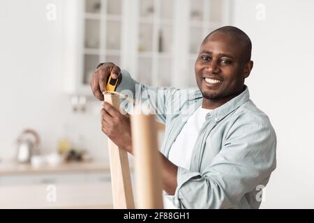 Homme de main afro-américain mesurant la largeur entre les pieds de la table en bois, en assemblant de nouveaux meubles à la maison Banque D'Images