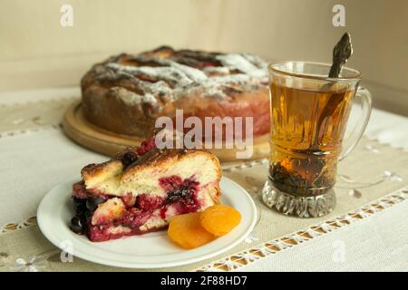 Chaussons de maman. Les chaussons sont prêts. Un morceau de gâteau sur une assiette sur le fond d'une tarte cuite et une tasse avec thé noir. Cuisson en quarantaine. Banque D'Images