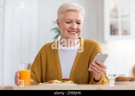 Femme âgée souriante utilisant un téléphone portable tout en déjeunant, en gros plan Banque D'Images