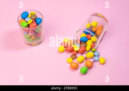 Bonbons au chocolat multicolores éparpillés dans deux verres sur fond rose.Haut vue sur le concept d'arrière-plan des bonbons créatifs et colorés avec espace de copie pour t Banque D'Images