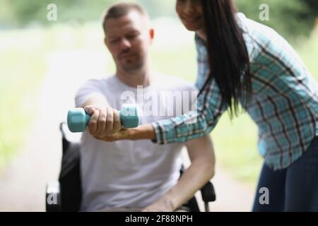 Infirmière aidant le jeune homme handicapé en fauteuil roulant à lever l'haltère gros plan Banque D'Images