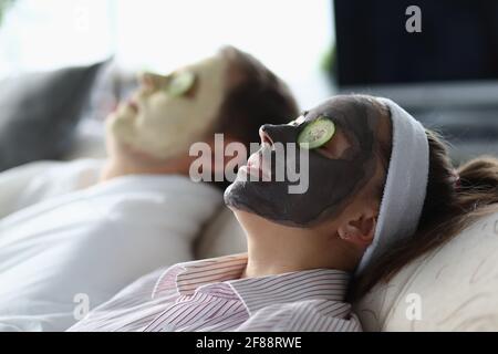 Jeune homme et femme allongé avec des masques cosmétiques sur leur les visages et les tranches de concombre sur les yeux Banque D'Images