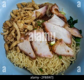 Gros plan de Noodle aux œufs avec tranches de porc rôti rouge et Wonton, porc croustillant avec craquelure croustillante dans un bol bleu. Cuisine chinoise cantonaise, vue sur le dessus, sel Banque D'Images