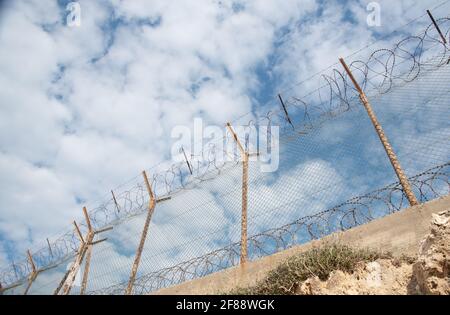 Clôture de sécurité avec fil barbelé contre un ciel bleu nuageux Banque D'Images