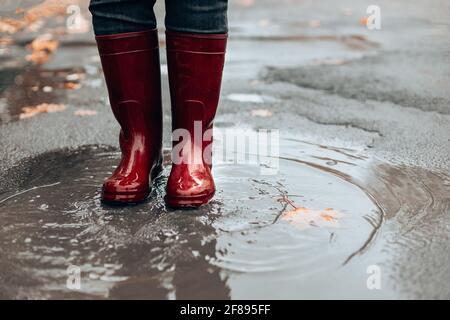 Femme avec des bottes en caoutchouc rouge foncé sautant dans le bas de la porte, gros plan. Temps pluvieux Banque D'Images