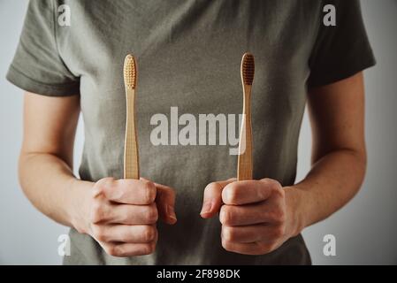 Femme en t-short vert tient des brosses à dents en bambou. Articles écologiques et concept zéro déchet Banque D'Images