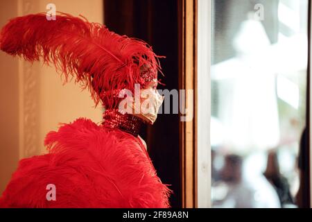 Une fille dans un masque et dans un costume rouge et une coiffe faite de plumes tient dans le profil Banque D'Images