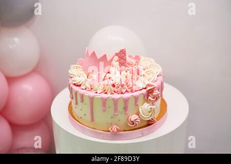 gâteau rose délicat avec boules, couronne de princesse dorée et numéro 1. Une fête d'anniversaire d'une fille d'un an avec gâteau et ballons d'hélium sur bac blanc Banque D'Images