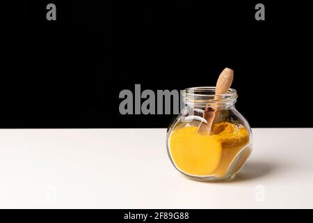 Poudre d'épices au curry dans un pot en verre et une cuillère en bois sur une table blanche. Banque D'Images