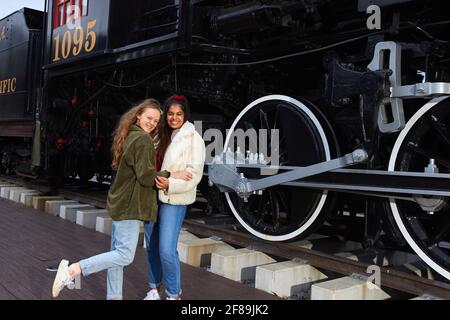 Deux filles sont les meilleures amies depuis la maternelle, se réunifier et avoir une soirée amusante se posant à côté d'un vieux train de locomotives à vapeur Banque D'Images